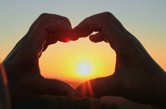 2 mains en forme de coeur qui entourent un soleil couchant